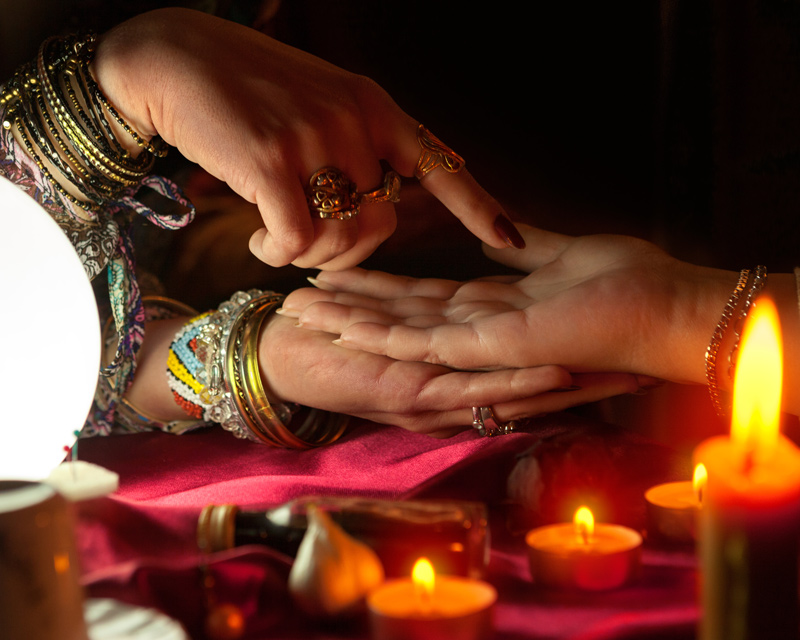 A psychic's hand is pointing to the lines on a woman's hand during a palm reading.