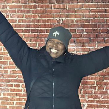 A happy middle-aged black woman with her arms in the air in celebration.